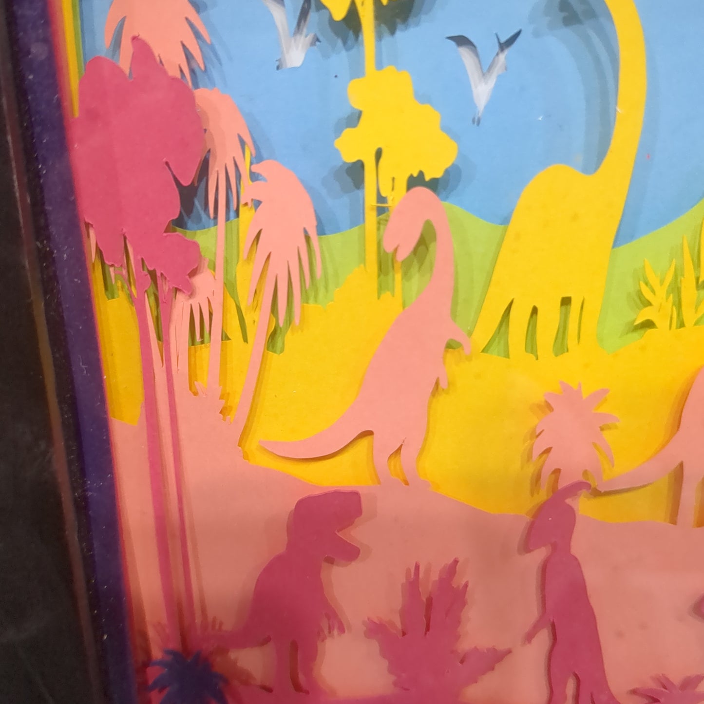 Roughly 8 x 6 x 1” black shadow box with a colorful paper cut dinosaur serene