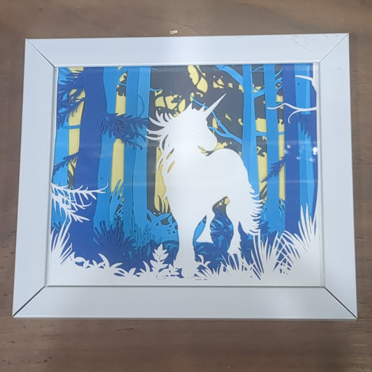 Roughly 5 x 6” white shadow box with paper cut unicorn in Forest serene