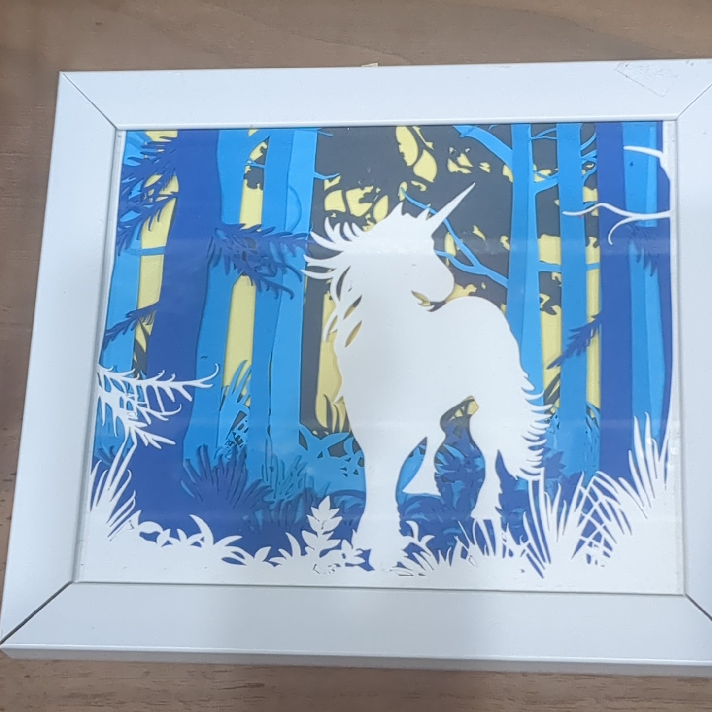 Roughly 5 x 6” white shadow box with paper cut unicorn in Forest serene