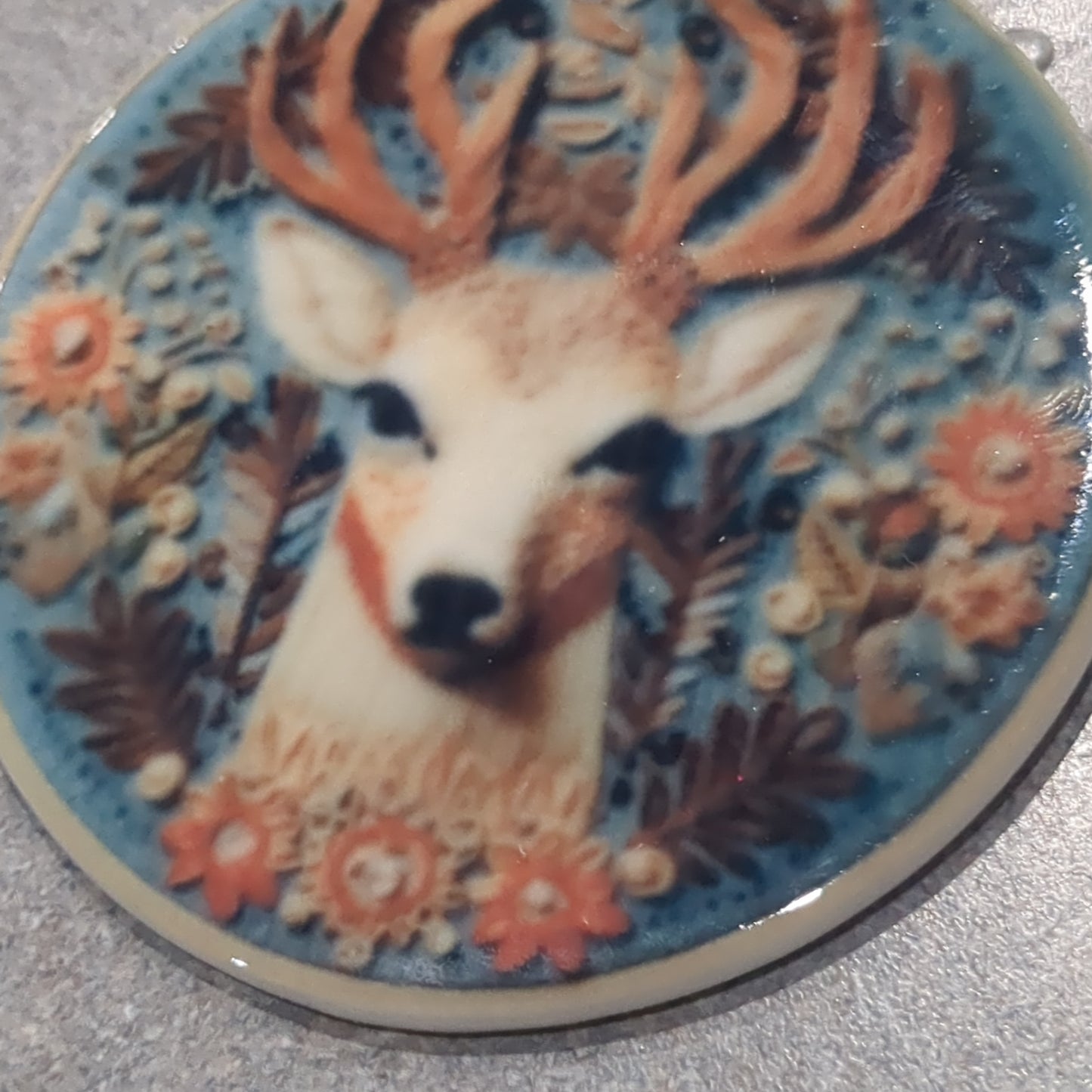 Ceramic ornament with a deer head surrounded by flowers and leaves, it appears 3D but it is not