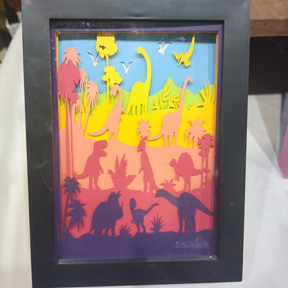 Roughly 8 x 6 x 1” black shadow box with a colorful paper cut dinosaur serene