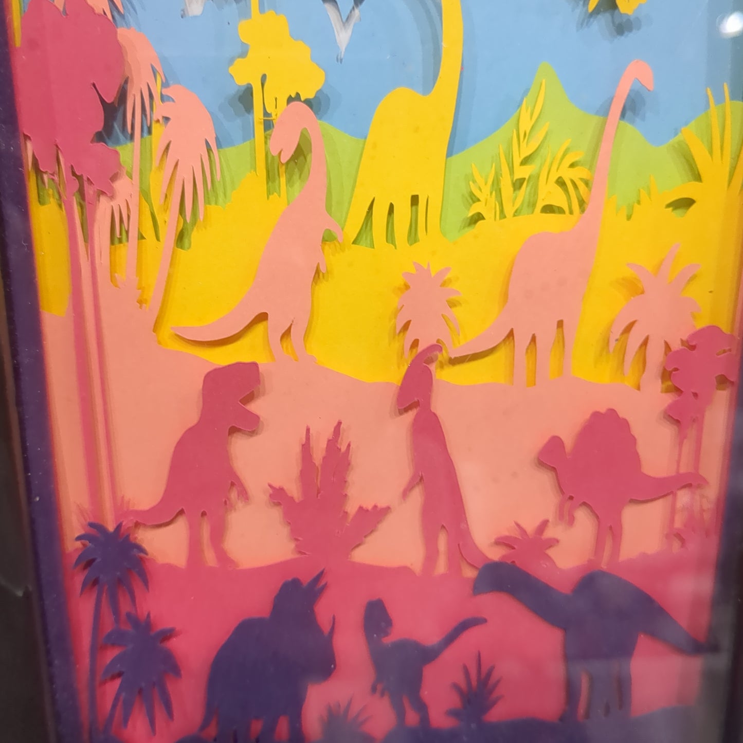 Roughly 8 x 6 x 1” black shadow box with a colorful paper cut dinosaur serene