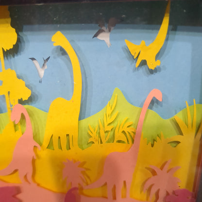 Roughly 8 x 6 x 1” black shadow box with a colorful paper cut dinosaur serene