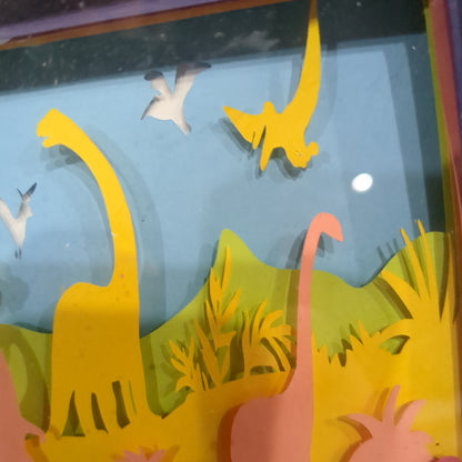 Roughly 8 x 6 x 1” black shadow box with a colorful paper cut dinosaur serene