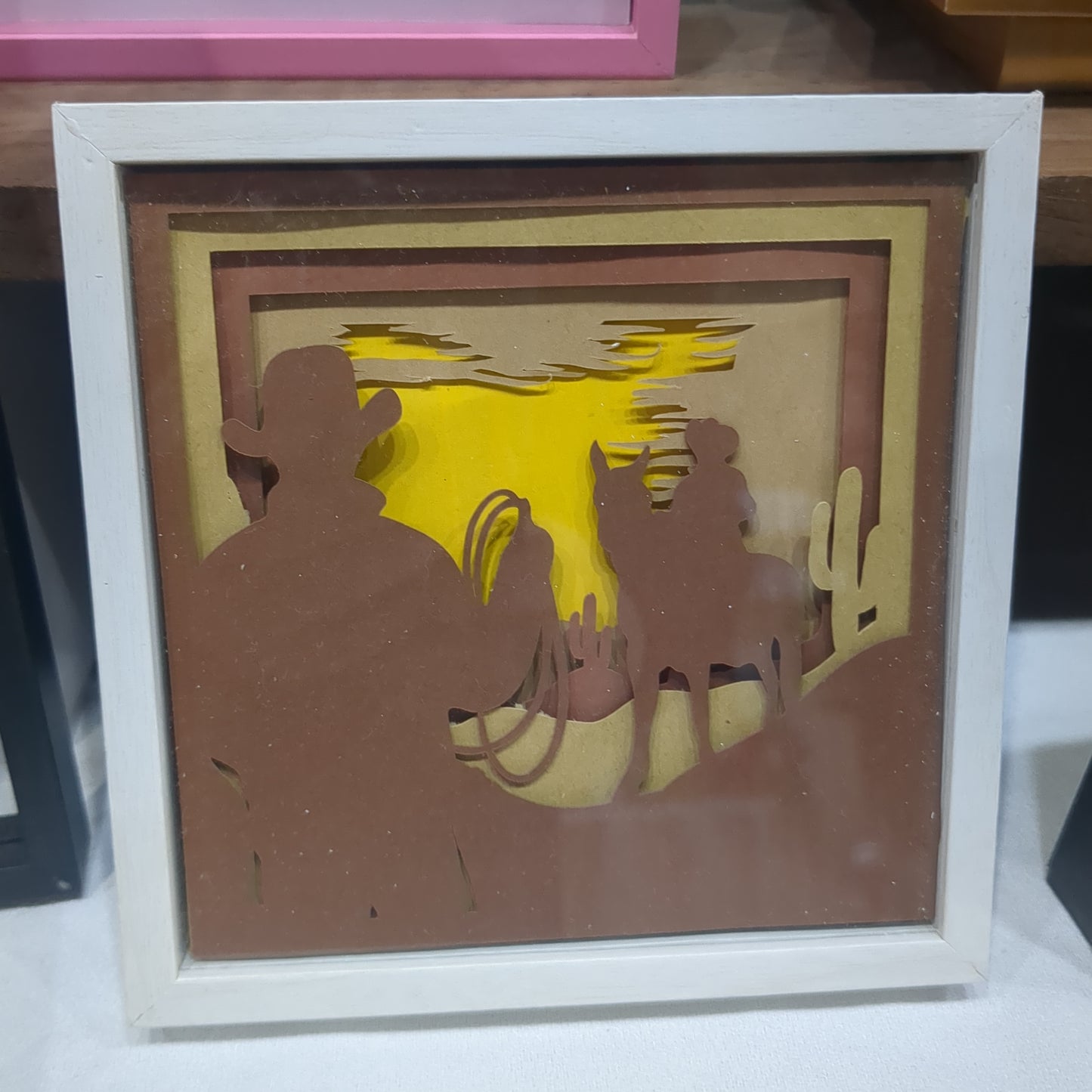 5 1/2 x 5 1/2” white shadow box with paper cut cowboy and dessert scene