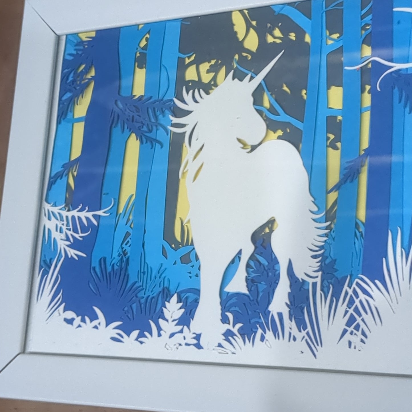 Roughly 5 x 6” white shadow box with paper cut unicorn in Forest serene